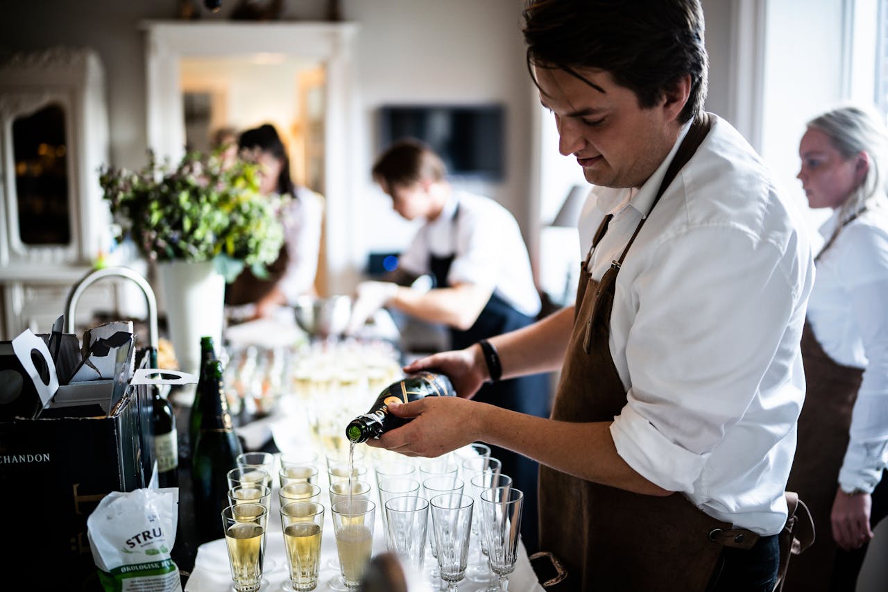 Waitstaff pouring champagne into glasses at a sophisticated indoor event.